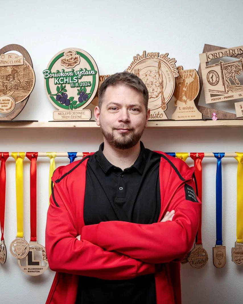 Martin Mařík, jednatel HOORAY s.r.o., se založenýma rukama před stěnou s dřevěnými medailemi a trofejemi